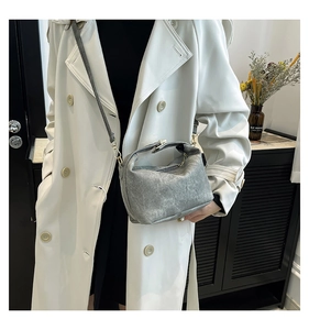 Detail of silver textured crossbody bag with adjustable strap on a white trench coat