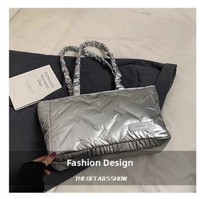 Detail of silver metallic quilted tote with ruffled straps on a grey suit and book