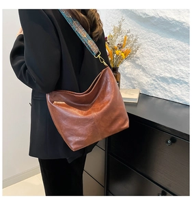 Close-up of caramel leather bucket bag featuring a colorful bohemian woven shoulder strap