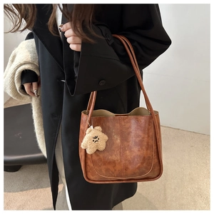 Close-up of a brown vintage leather bucket bag featuring a khaki star plush charm detail
