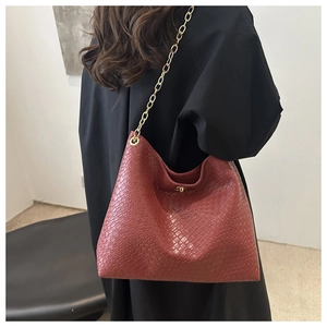 Detail of dark red woven hobo bag with sleek chain strap shown on a model