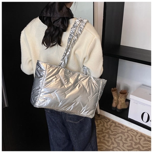 Quilted silver tote bag in puffer style shown on shoulder to display size and fit