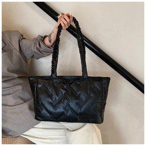 Detail of black quilted tote bag featuring a ruffled scrunchie handle and logo patch