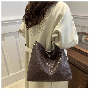 Detail of dark brown woven tote bag with gold chain strap and metallic closure