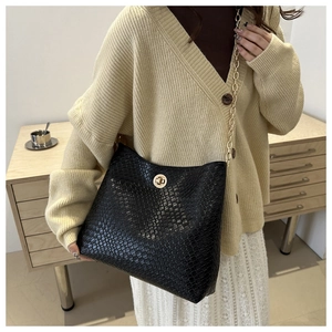 Detail of black faux leather crossbody bag with crocodile texture and gold chain strap