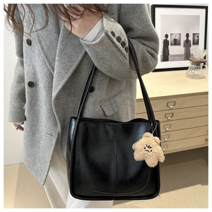 Detail of black leather tote bag with vertical stitching and brown star plush charm