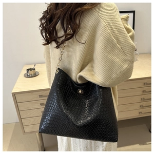 Close-up of black textured tote bag with golden chain strap and round metal twist lock