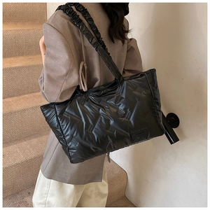 Detail of black quilted tote bag with unique ruched shoulder strap and glossy finish