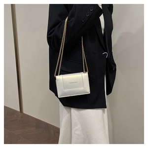 Close-up of pearl white square chain bag featuring a gold fashion logo on black blazer
