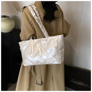 Macro detail of silver quilted puffer tote bag with metallic sheen and pleated shoulder strap
