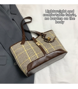 Detail of plaid tote bag with leather straps and golden clasp on a gray blazer