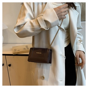 Detail of dark brown leather mini bag with gold chain strap on white coat