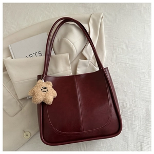 Detail of burgundy leather tote bag with vertical stitching and plush bear charm