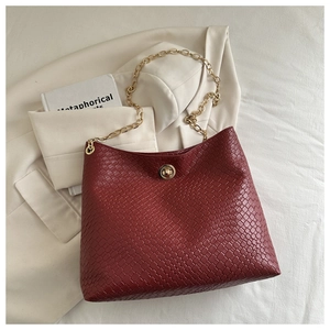 Detail of red-brown woven tote bag with chunky gold chain strap and metal twist lock