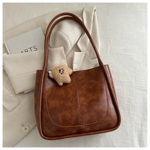 Detail of vintage brown leather tote bag texture with cute plush bear charm on a blazer