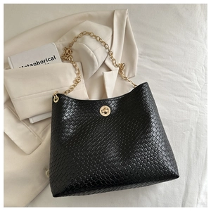 Detail of black woven texture tote bag featuring a gold chain strap and metal rotary lock