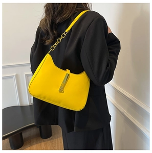 Detailed side view of yellow half-moon underarm bag with gold chain on black blazer