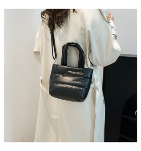 Detail of black quilted puffer bag in glossy nylon fabric worn with a trench coat