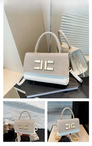 Macro shot of white leather handbag featuring a gold geometric buckle and rhinestone panel