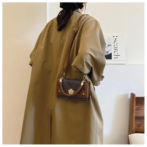 Détail du sac bandoulière vintage avec fermoir fleur porté sur un trench-coat beige classique