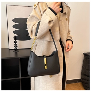 Detail of minimalist black leather underarm bag with gold metal lock and chain strap
