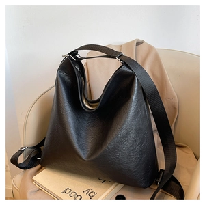 Vue détaillée d'un grand sac cabas en cuir noir posé sur un fauteuil dans un décor sobre
