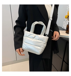 Detail of white quilted puffer tote with knotted handle and wide canvas strap on a model