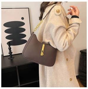 Detail of dark brown leather crescent bag featuring a gold metal lock and chain strap