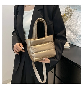 Detail of champagne gold quilted bucket bag with wide top handle and white crossbody strap