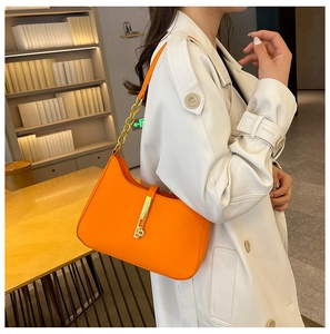 Detail of orange hobo bag with gold chain strap and metal lock worn with a beige trench coat