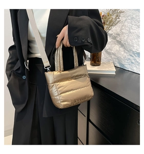 Close-up of golden quilted puffer bag with fabric strap worn on a black blazer