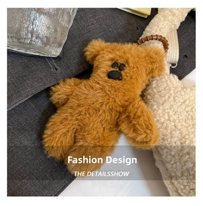 Detail view of a fluffy brown bear keychain charm on a white plush bucket bag