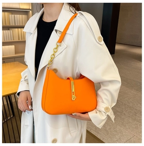 Detail view of bright orange leather shoulder bag with gold clasp and chain strap