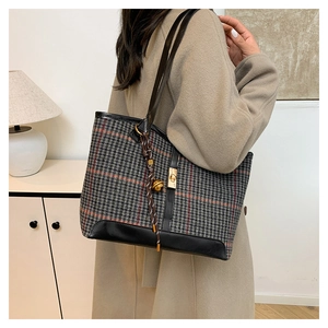 Detail of plaid wool tote bag with black leather straps and gold buckle on a model