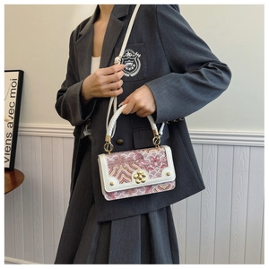 Détail du mini sac bandoulière avec fermoir fleur dorée et poignée tressée sur blazer