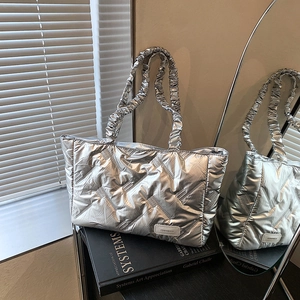 Silver quilted tote bag with ruched strap and metallic finish on an art book background