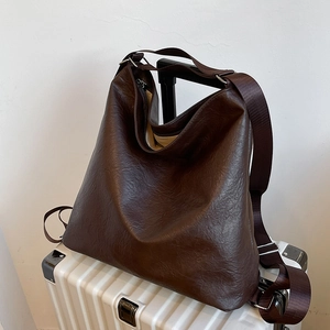 Grand sac hobo marron foncé avec texture plissée rétro sur une valise blanche