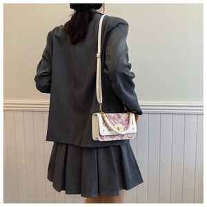 Détail d'un sac floral blanc et rose avec un fermoir fleur dorée et une poignée tissée