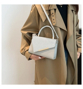 Close-up of grey crossbody bag with silver glitter flap and gold metal bar on trench coat