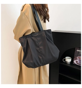 Detailed view of black pleated nylon tote bag with fashion patch on shoulder strap