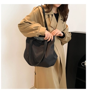 Detail of minimalist black nylon tote bag with Fashion label worn over a khaki trench coat