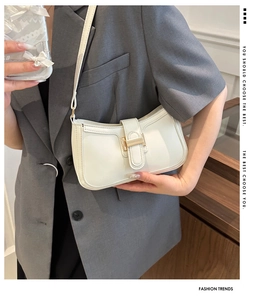 Close-up of white leather square shoulder bag with gold metal clasp on a grey blazer