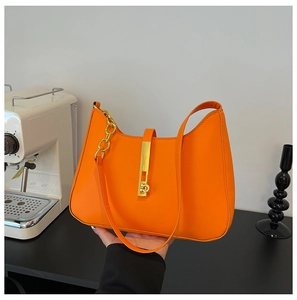 Detail of a bright orange crossbody bag with bold gold chain and sleek metallic lock buckle