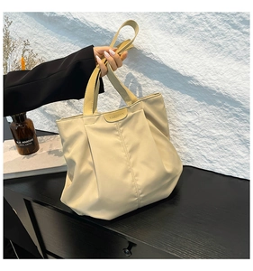 Detail of beige pleated tote bag with FASHION label held by hand in a minimalist setting