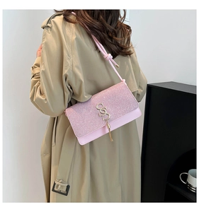 Pink sequined shoulder bag with gold letter logo and tassel shown on a stylish trench coat