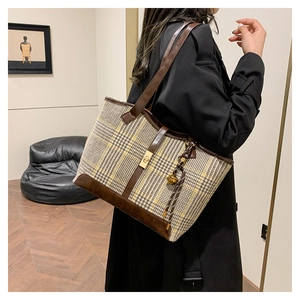 Model showing a large plaid tote bag with brown leather straps and gold twist-lock closure