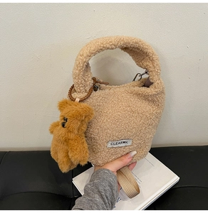 Detail of khaki plush faux fur bucket bag featuring bear charm and clear brand label