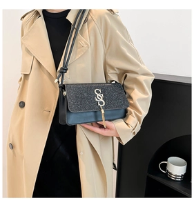 Detail view of a black flap bag featuring shimmering sequins and a gold tassel charm