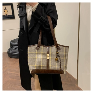 Detail of wool houndstooth tote bag with brown leather handles and gold bell charm accessory