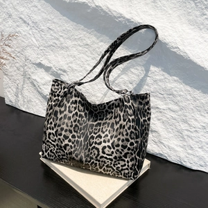 Large leopard print tote bag with long straps on white books against stone wall